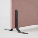 Närbild hörn av ljudabsorberande golvskärm i rosa klädsel, med svarta skärmfötter.
